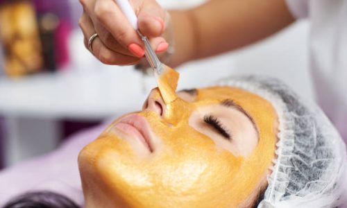 Macro photography of the hand of the beautician with the help of a special brush puts on the face of the girl a golden mask in the spa